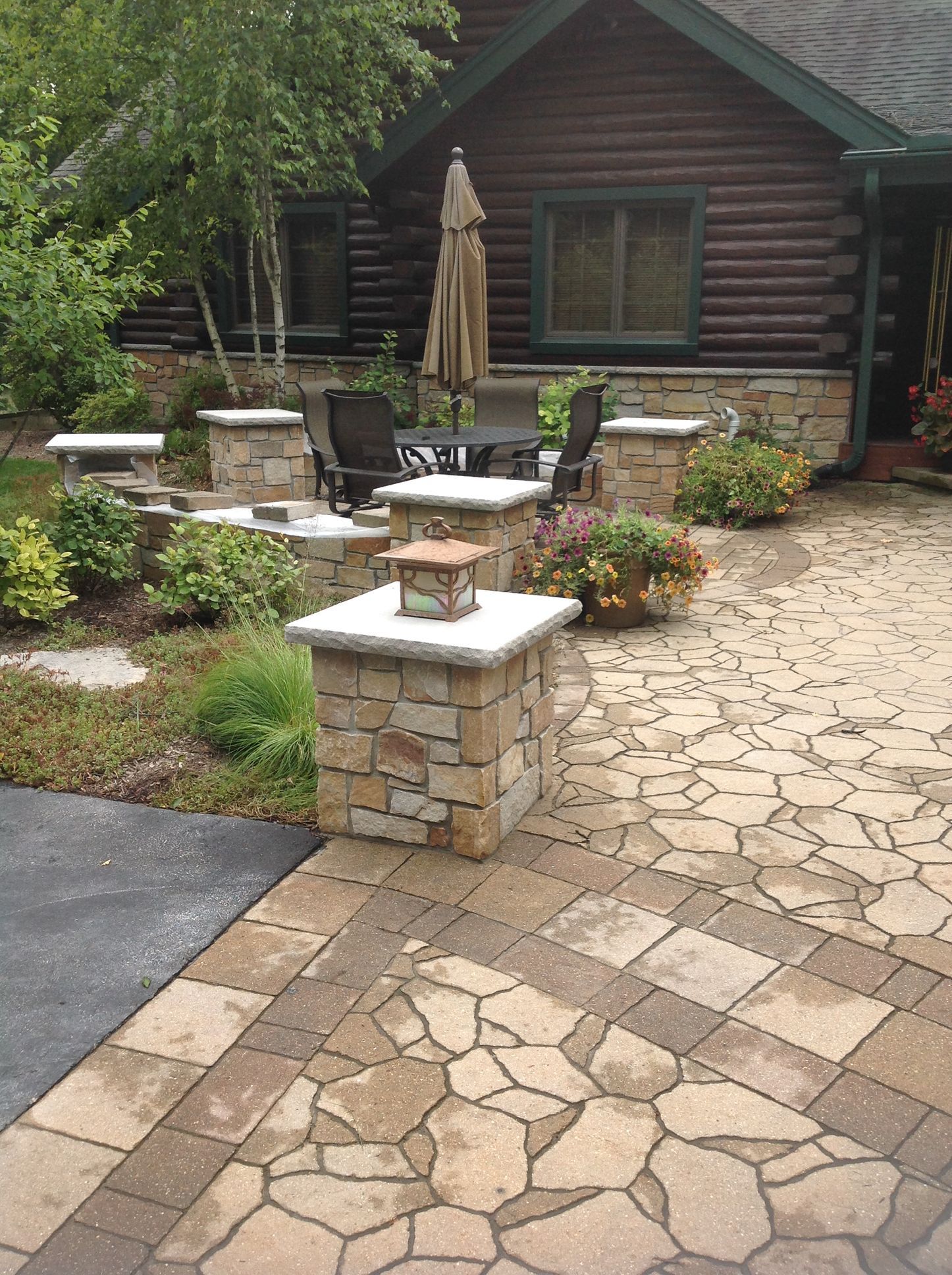A stone patio with decorative pillars and a dining area outside a rustic log cabin home.