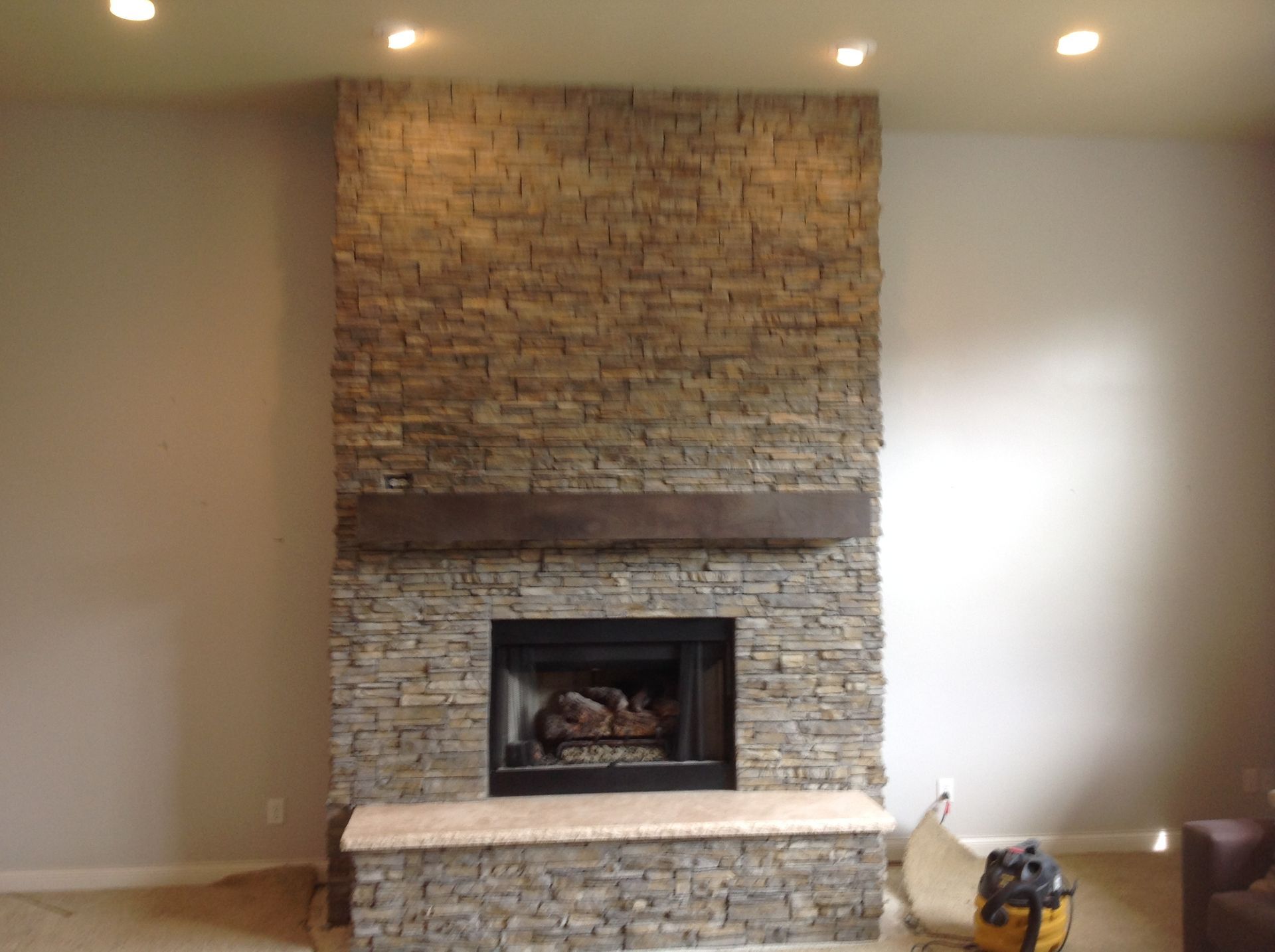 A floor-to-ceiling fireplace with stacked stone veneer, a wooden mantel, and a raised stone hearth in a living room.