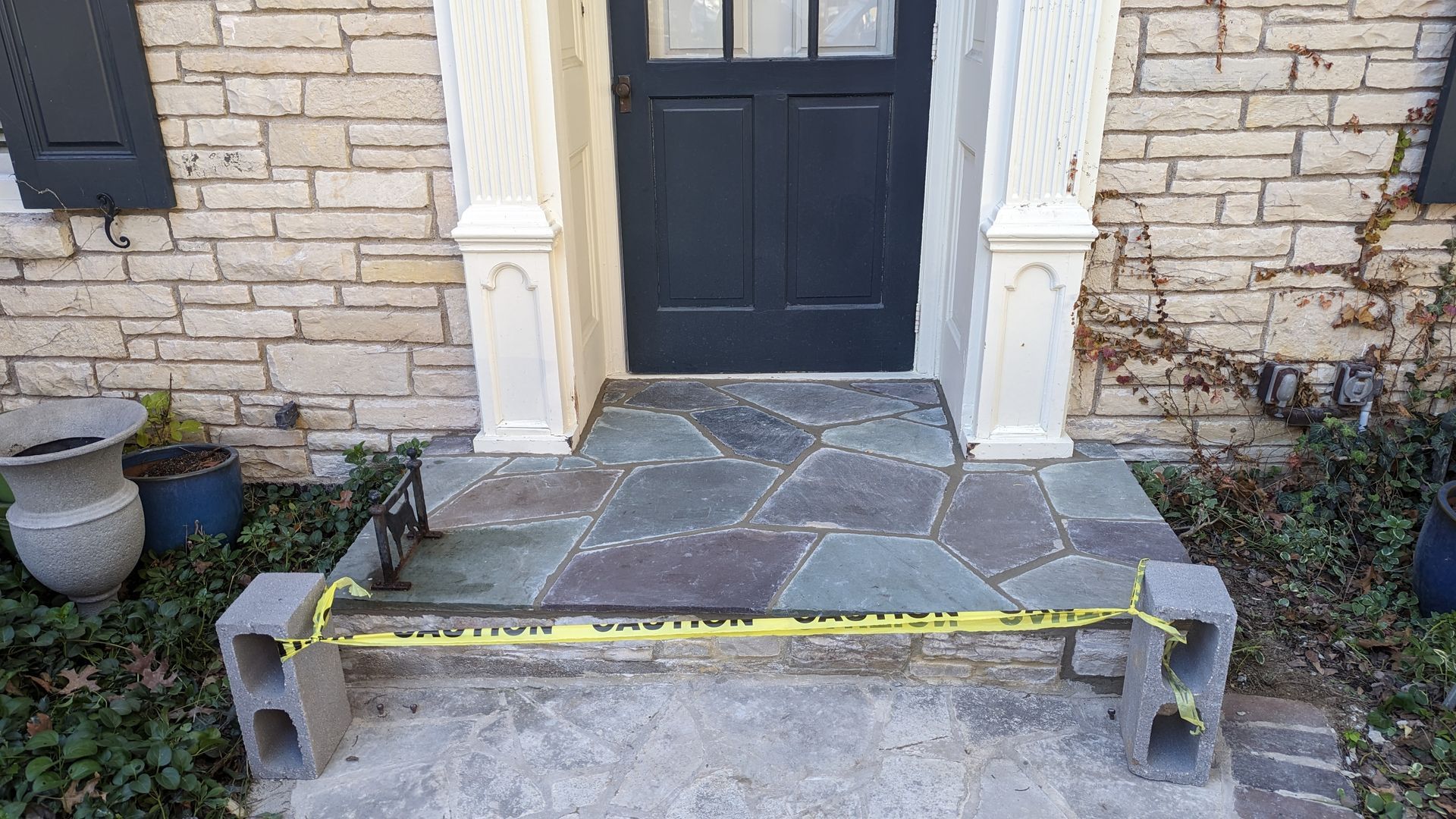 A stone porch entry blocked by a yellow caution tape strung between two concrete blocks on the ground.