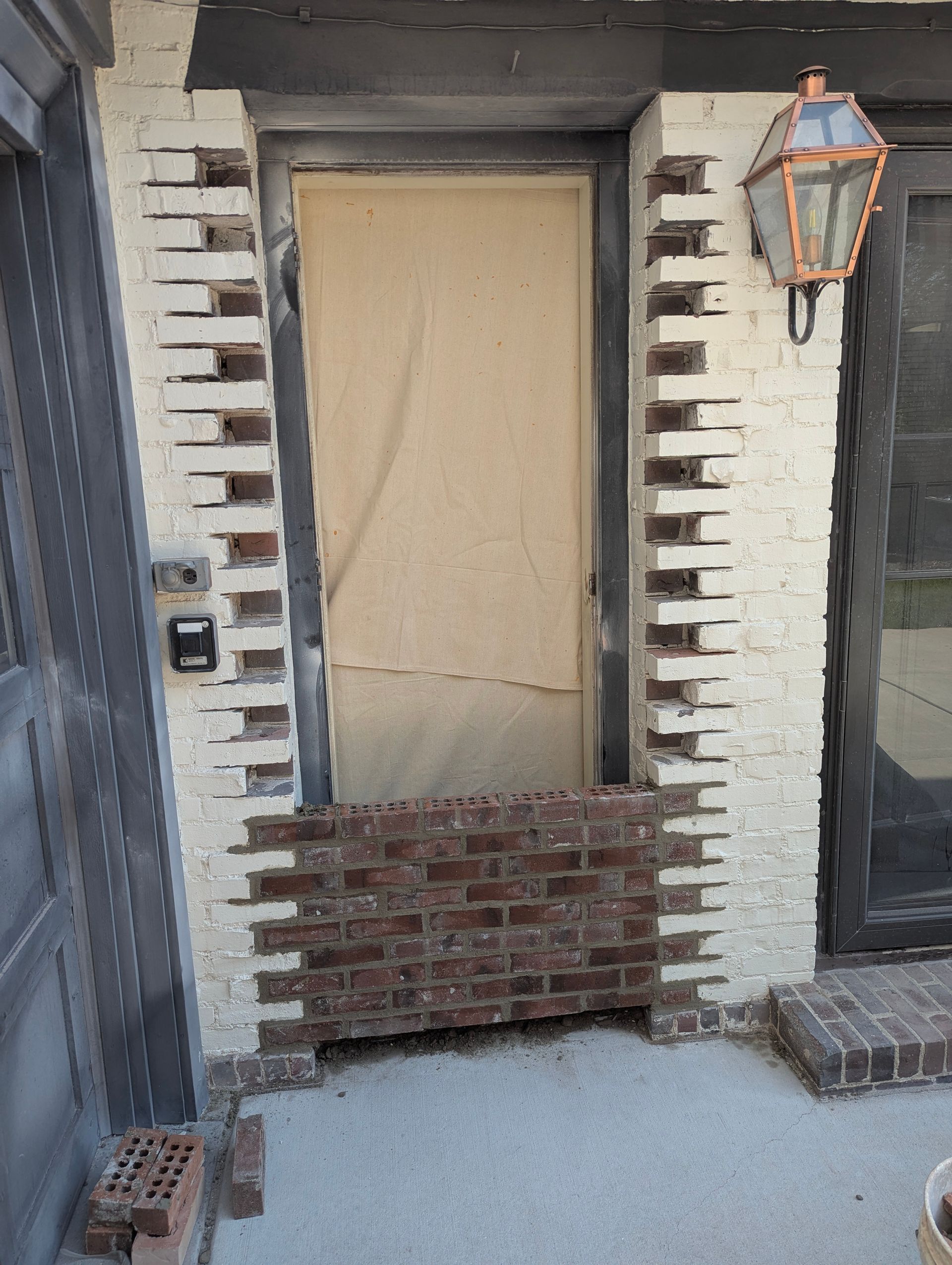 A doorway with a light-colored paper covering, partially filled with red brick in a recessed brick wall.