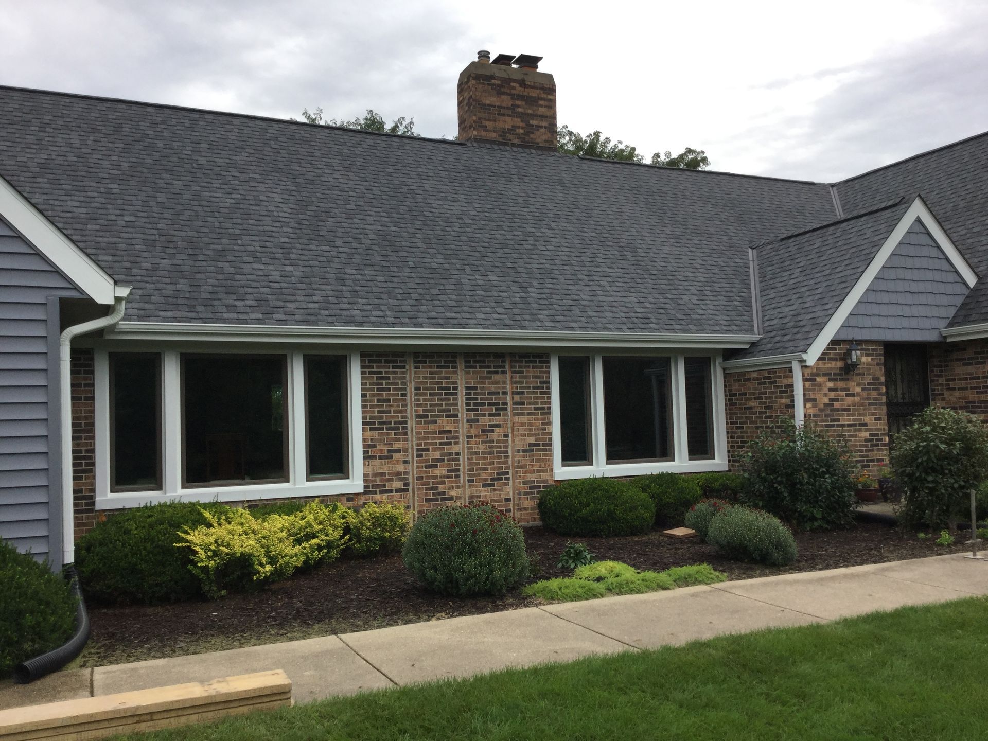 A single-story house with dark shingle roofing, stone-clad walls, and a sidewalk leading to the front entrance.
