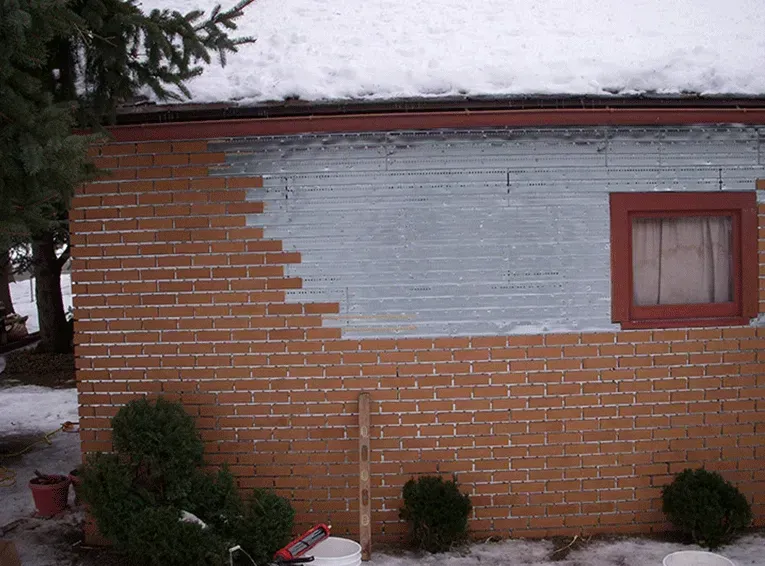 A brick wall partially painted grey, featuring a window with a reddish-brown frame, outdoors during winter.