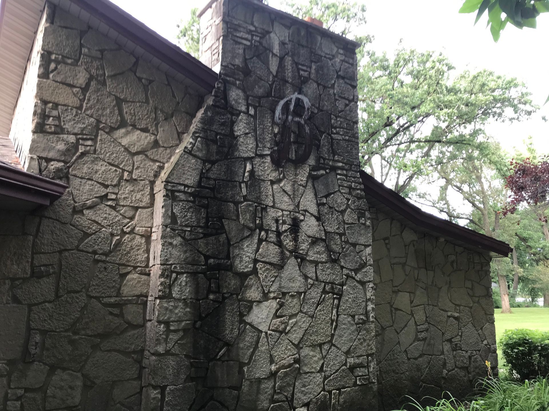 A stone chimney and exterior wall of a house with a dark, decorative circular emblem mounted near the top.