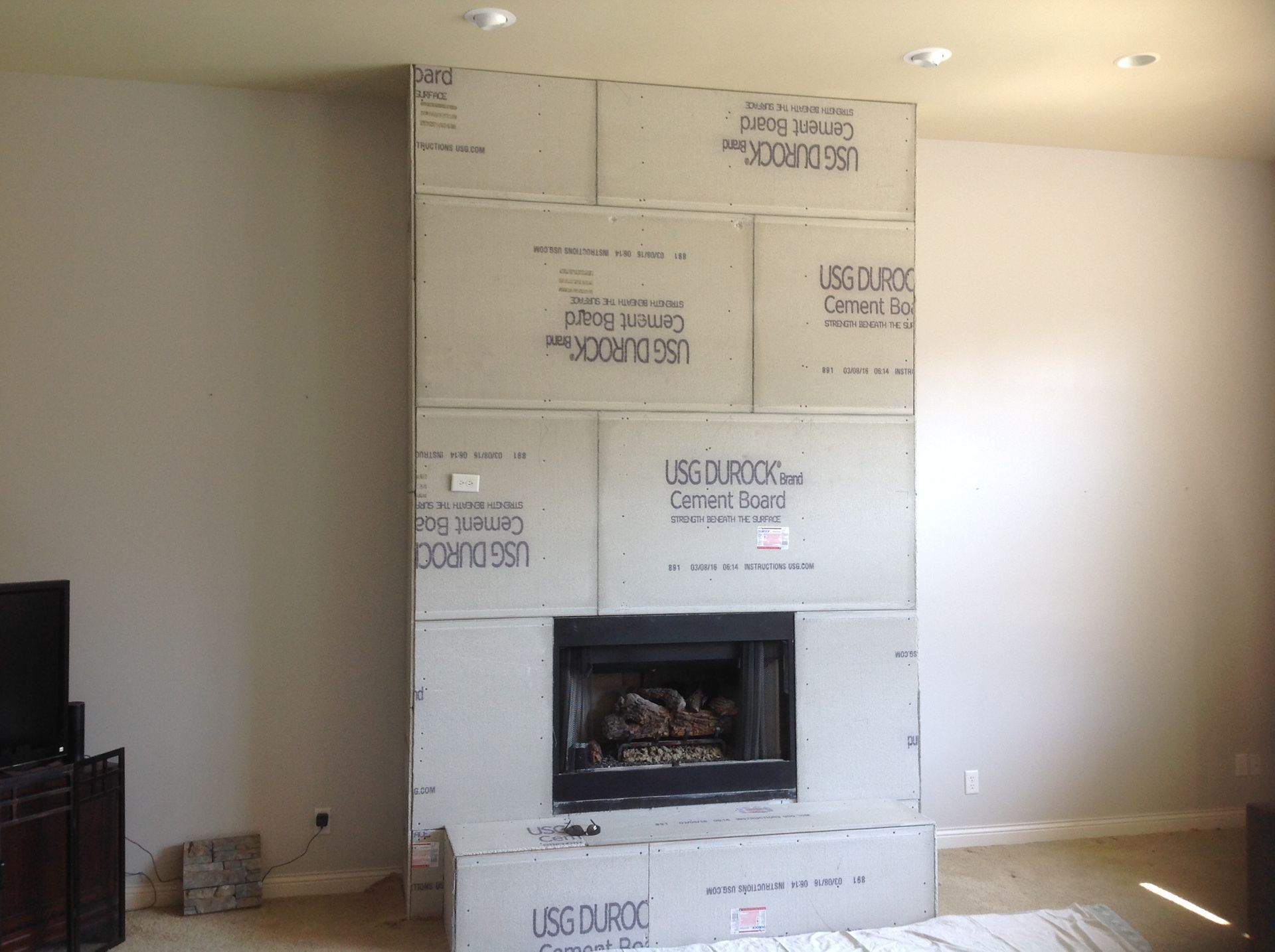 A fireplace surround in a living room, currently undergoing renovation with unfinished cement board panels installed.