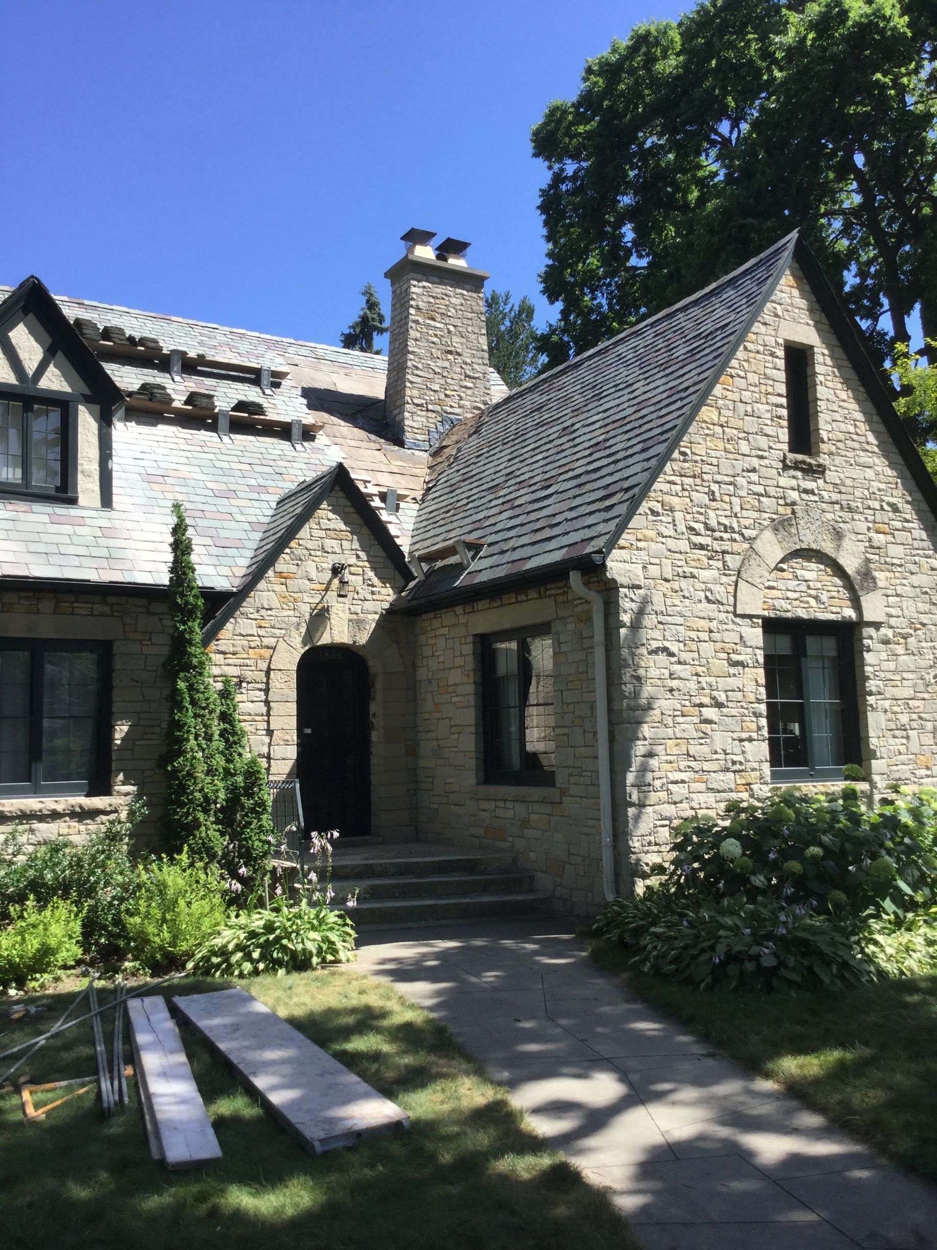 A stone Tudor-style house with a slate roof, dark window frames, and a walkway leading to a black front door.