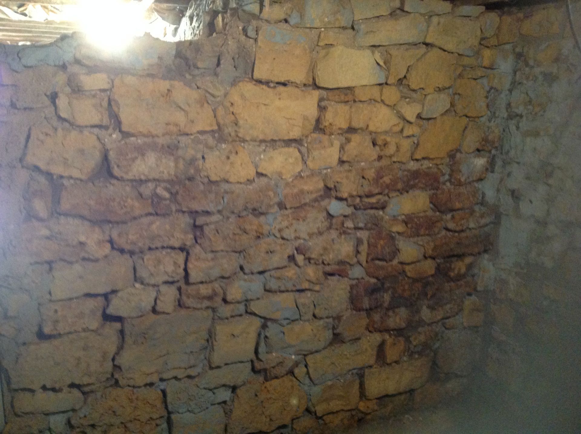 A weathered wall made of stacked, uneven, light brown stone blocks with visible gaps filled with mortar.