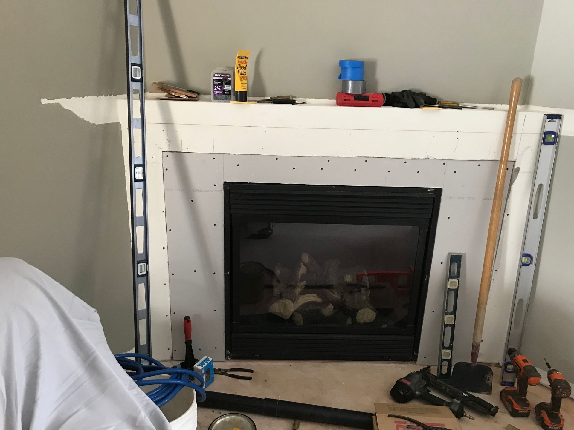 A fireplace undergoing renovation with drywall installed around the unit, tools, and levels resting on the mantle.