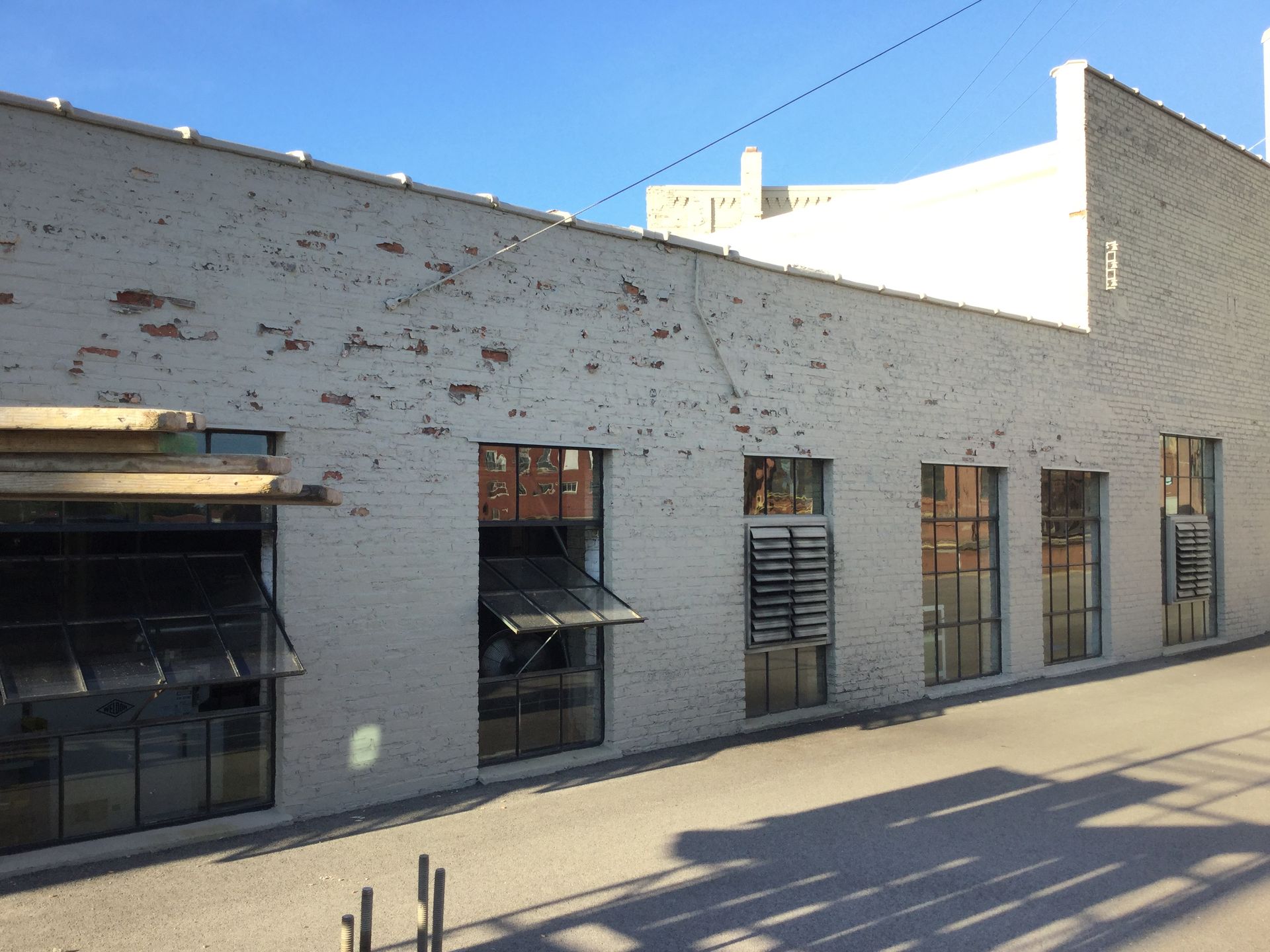 A side view of a white brick building with multiple large, dark-framed windows under a clear blue sky.