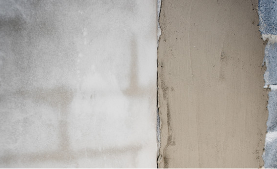 A split view of a cinder block wall, showing a smooth, finished section on the left and fresh, wet plaster on the right.