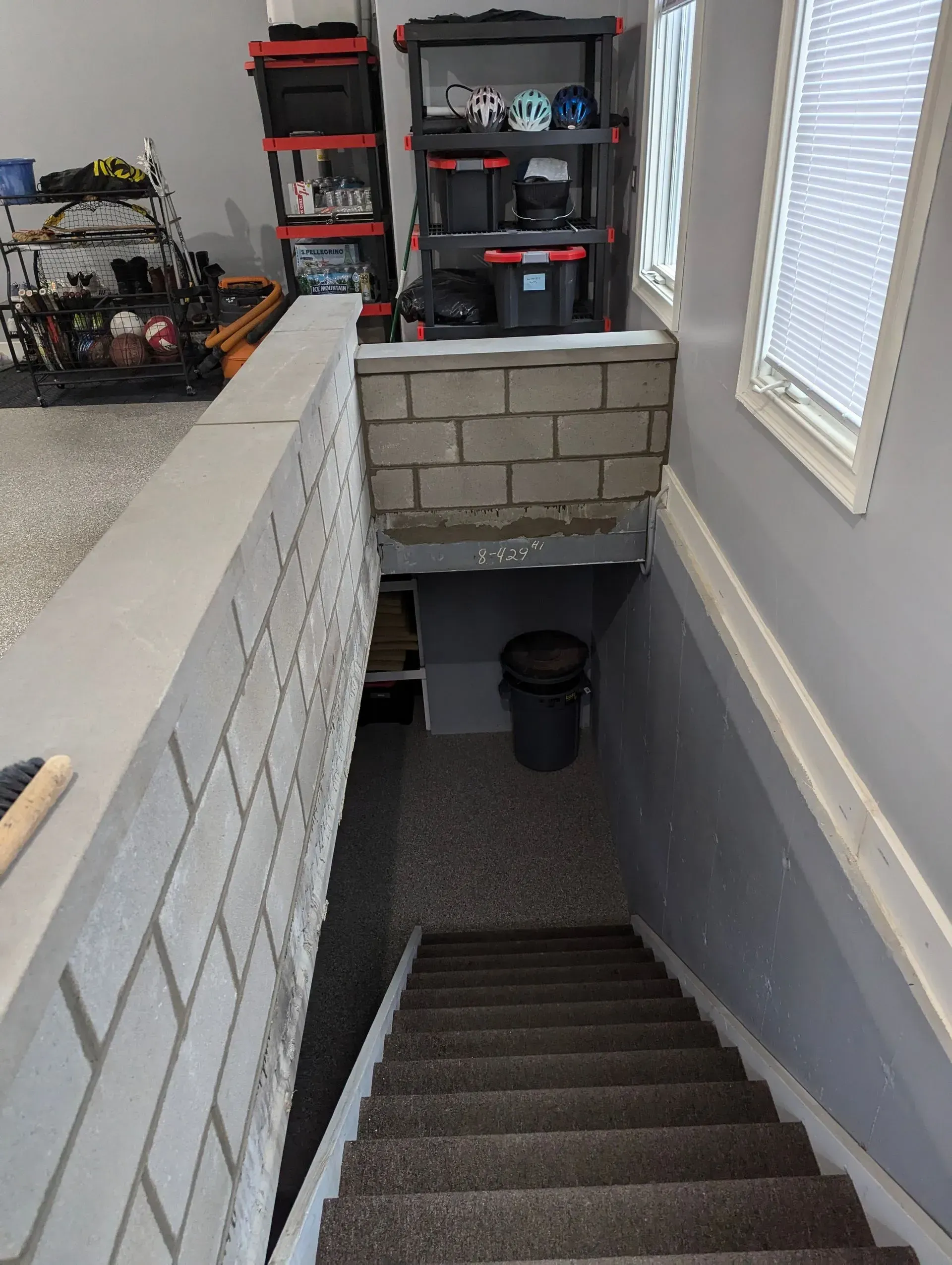 Looking down a carpeted staircase in a basement or garage with cinder block walls and storage shelving above.