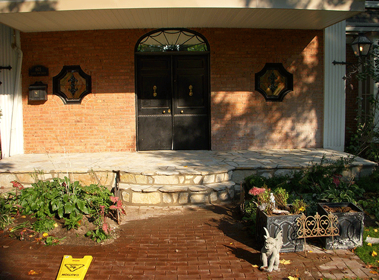 An arched double-door entryway with a brick exterior, stone porch, and landscaping in front.