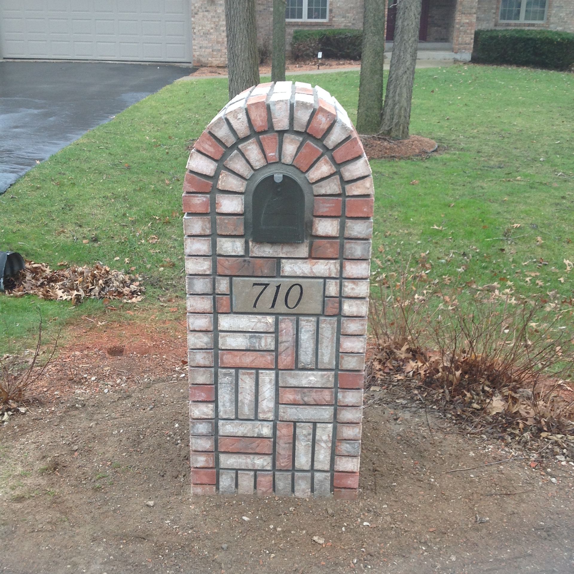 A brick mailbox with an arched top, featuring the house number 710, situated on a residential lawn.