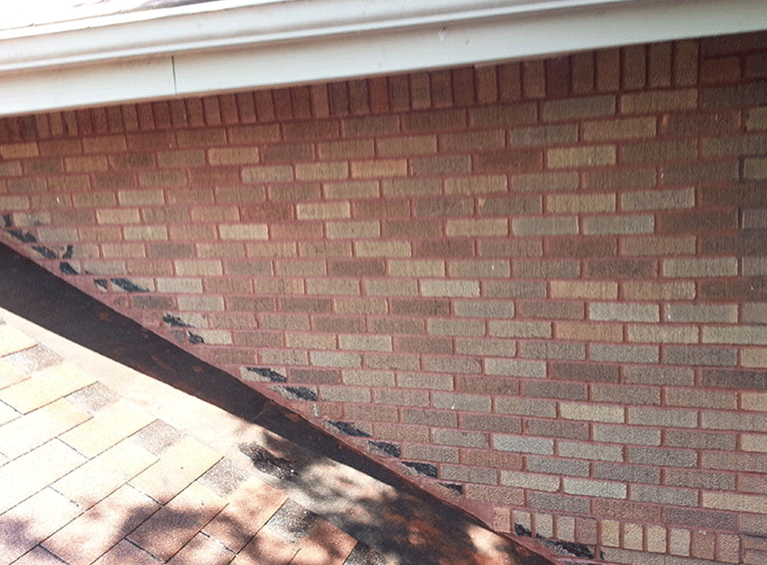 A low-angle view of a brick wall meeting a shingled roof with flashing and a gutter visible at the top.