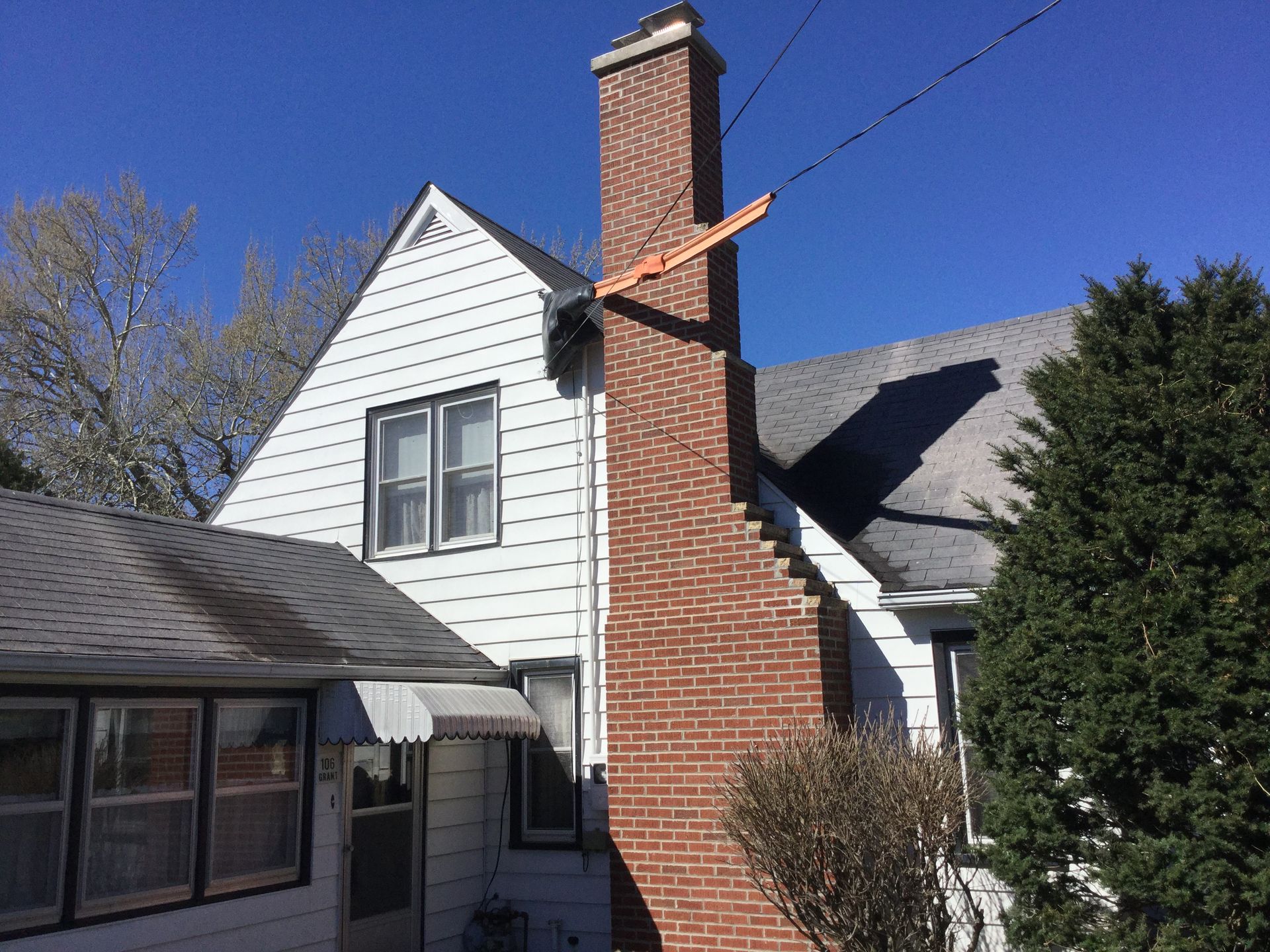 A red brick chimney rises alongside a white house with white siding, under a clear blue sky.