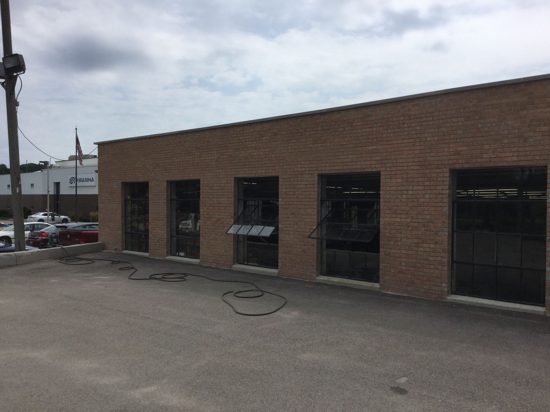 A low, tan brick commercial building with five large windows under a cloudy sky.