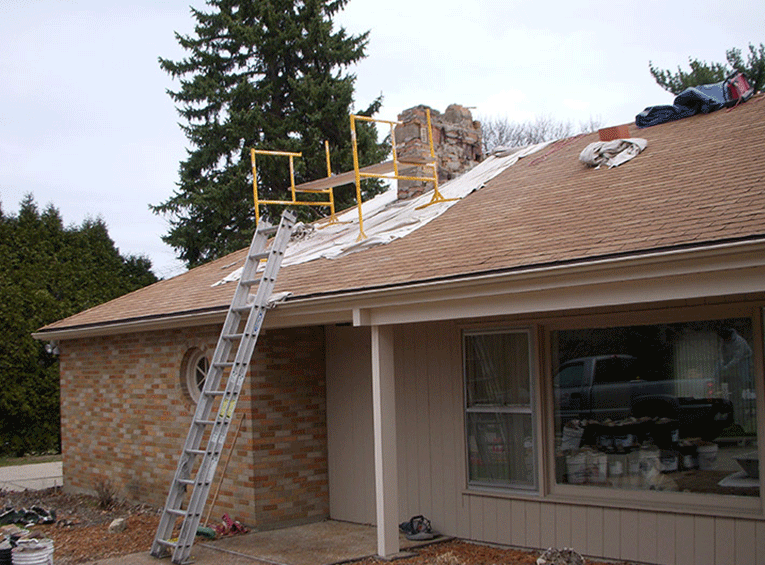 Scaffolding and a ladder set up on the roof of a one-story brick house to perform repairs on a chimney.