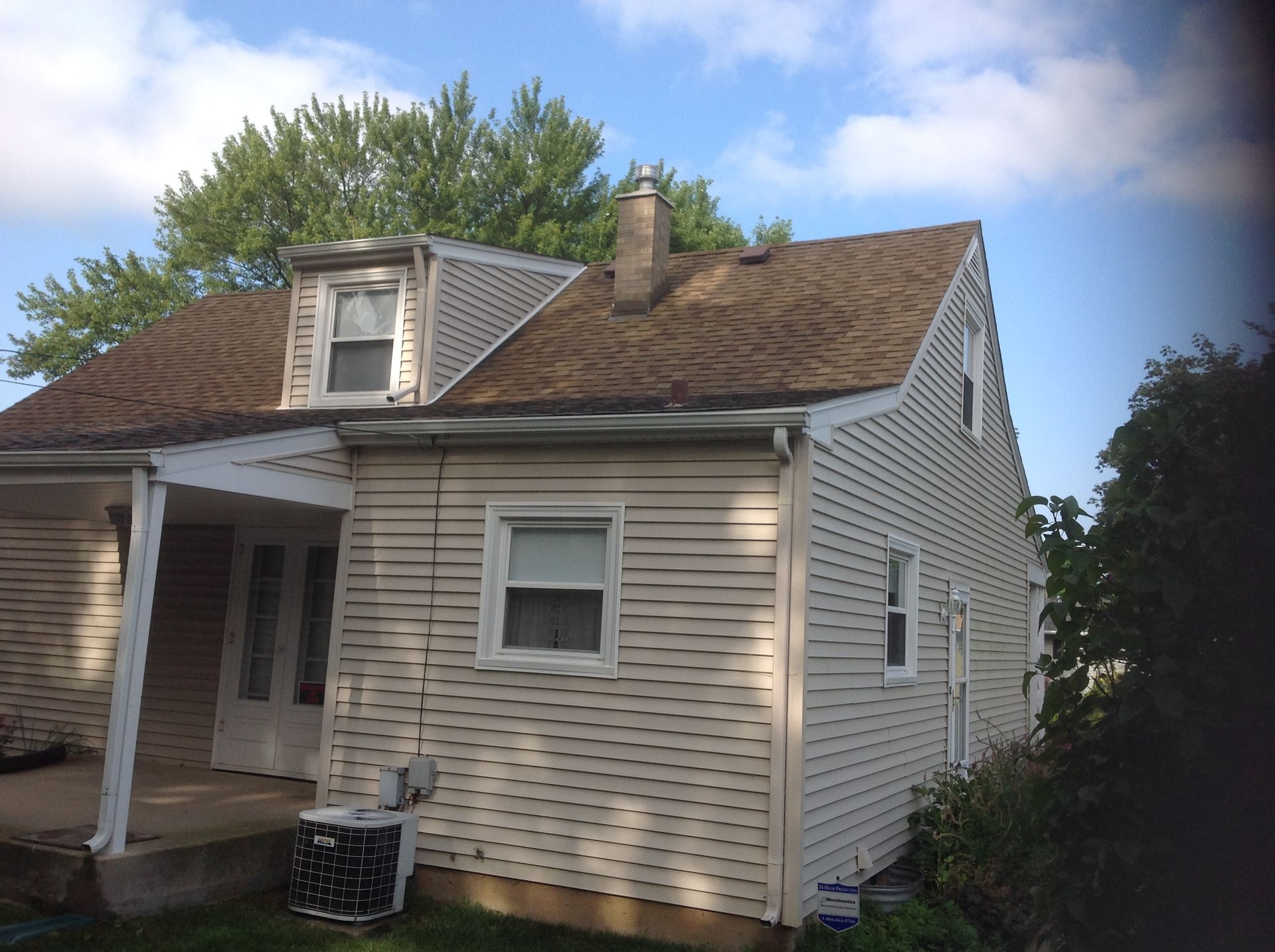 A light-colored house with weathered siding and a shingled roof under a blue, partly cloudy sky.