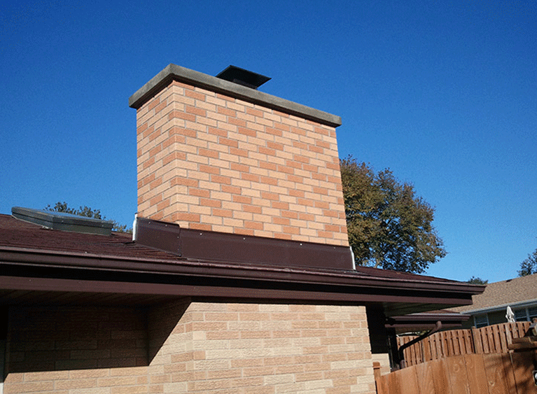A light-colored brick chimney sits on a brown roof against a clear blue sky.