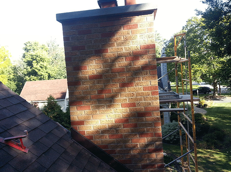 A brick chimney on a house roof viewed from above, with metal scaffolding set up against its side.