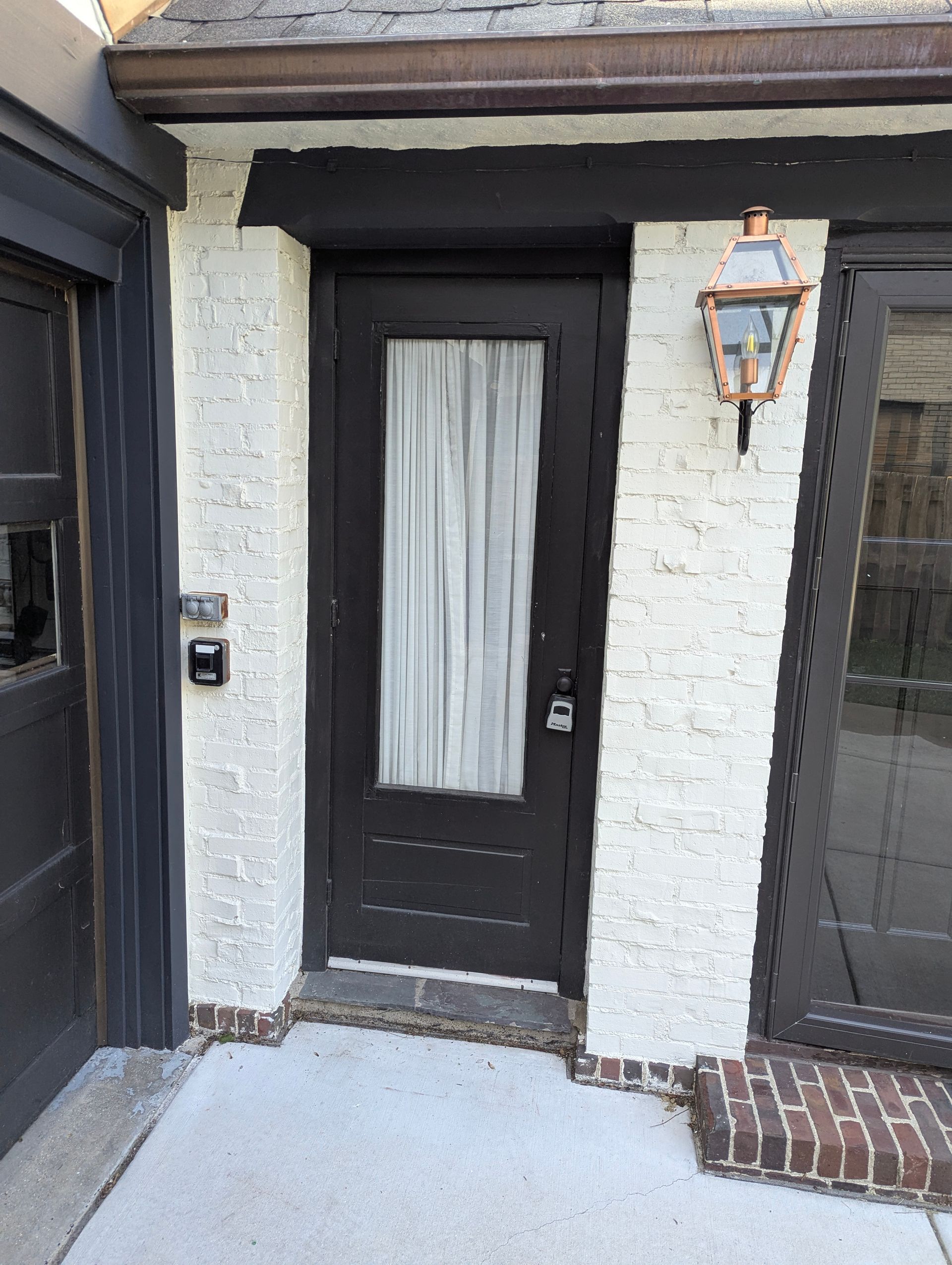 A dark brown entry door with a frosted glass window, set in a white painted brick wall next to a porch light.