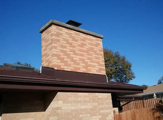 Brick chimney above a brown roof under a clear blue sky.