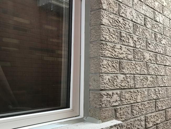 Close-up of a window beside a textured brick exterior wall and ledge.