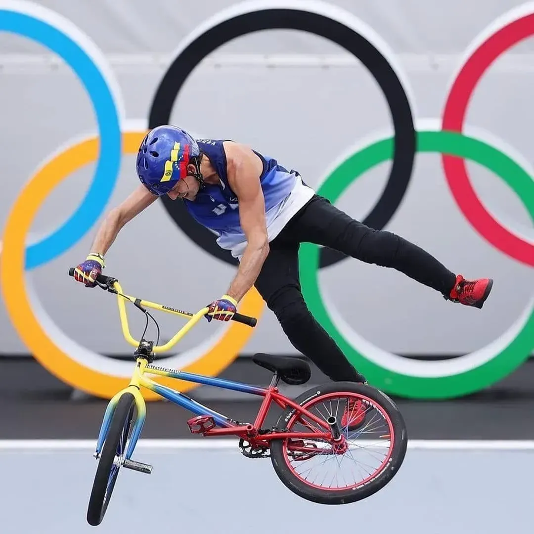 BMX cyclist in mid-air, performing a trick in front of the Olympic rings.