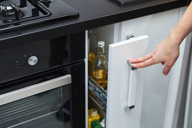 Person opening a kitchen cabinet holding cooking oil bottles, next to oven.