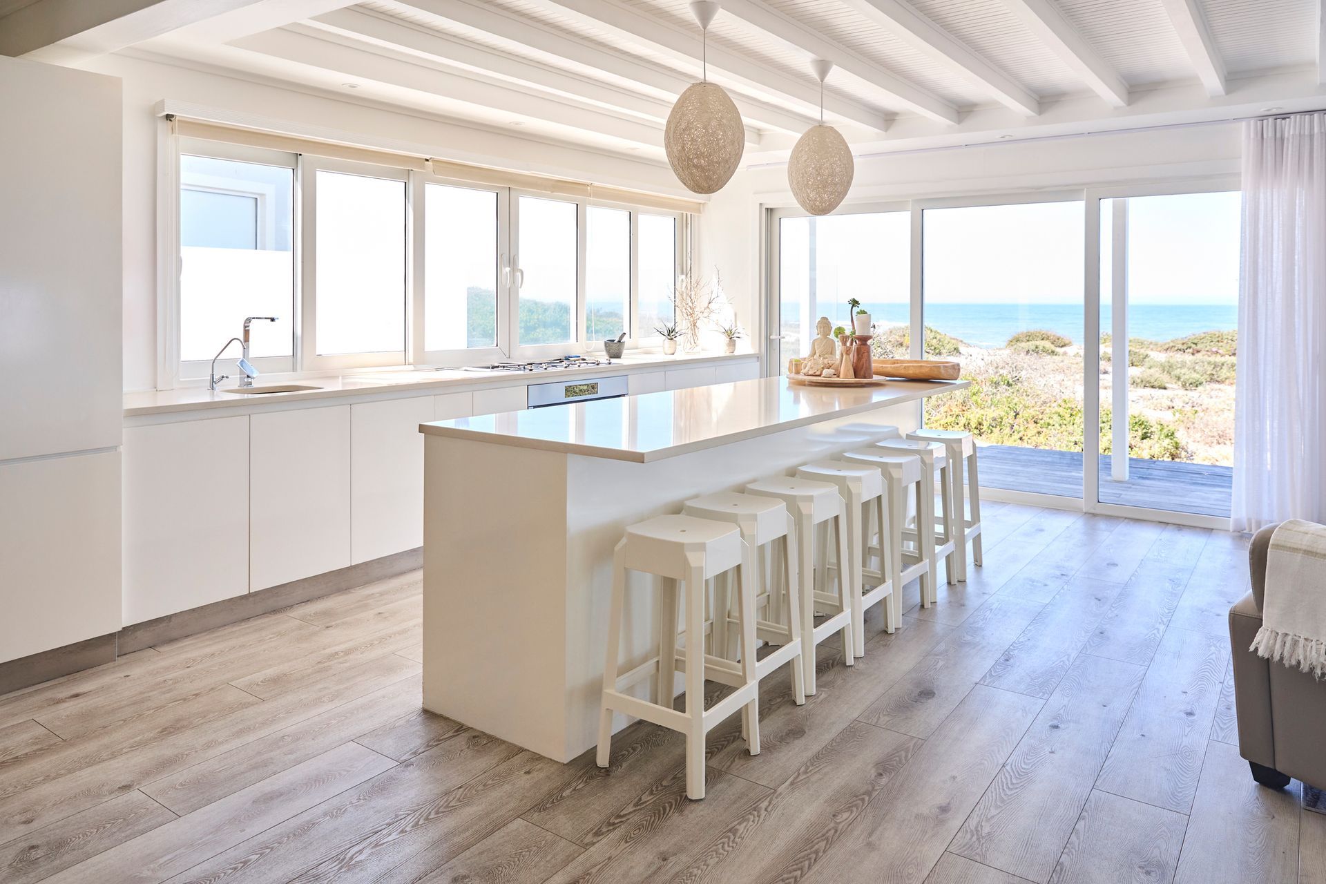 White kitchen with island, stools, and ocean view through large windows.
