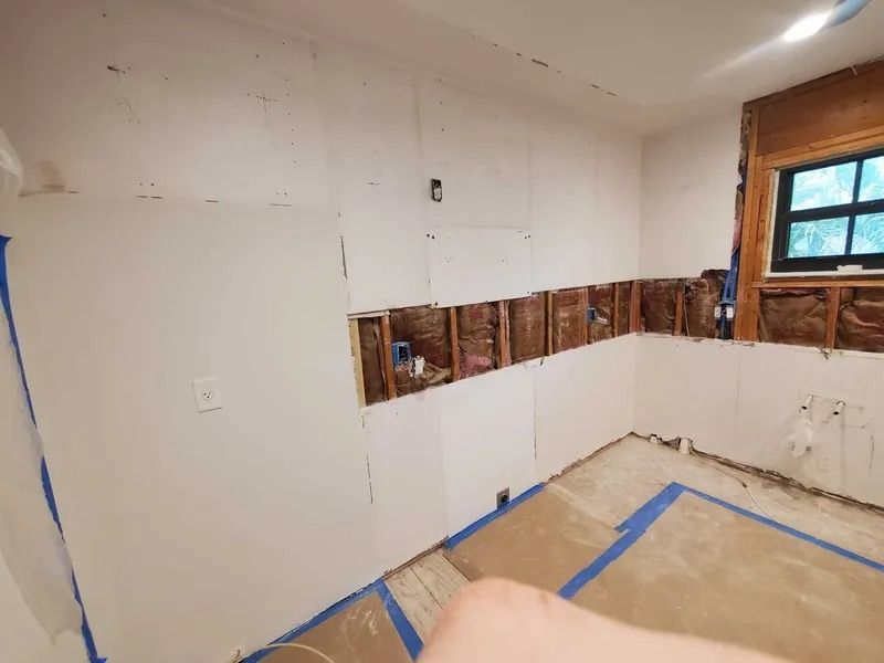 Kitchen renovation in progress; exposed studs, partial drywall, window, electrical boxes, and blue tape on floor.