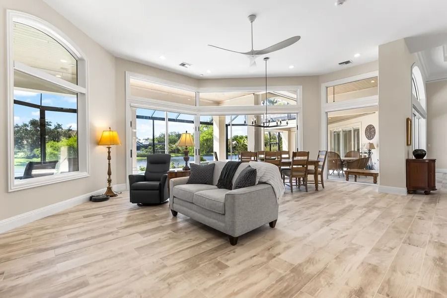 Bright living room with gray sofa, black chair, dining table, and large windows.