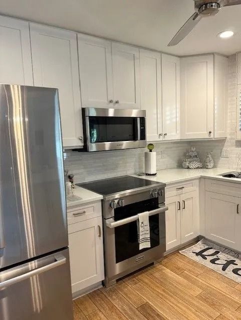 White kitchen with stainless steel appliances and wood flooring.