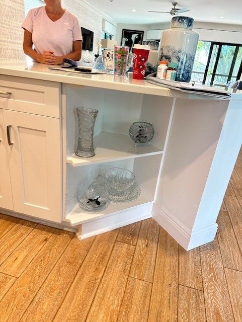 White kitchen island with open shelves displaying glassware. A person stands at the counter.