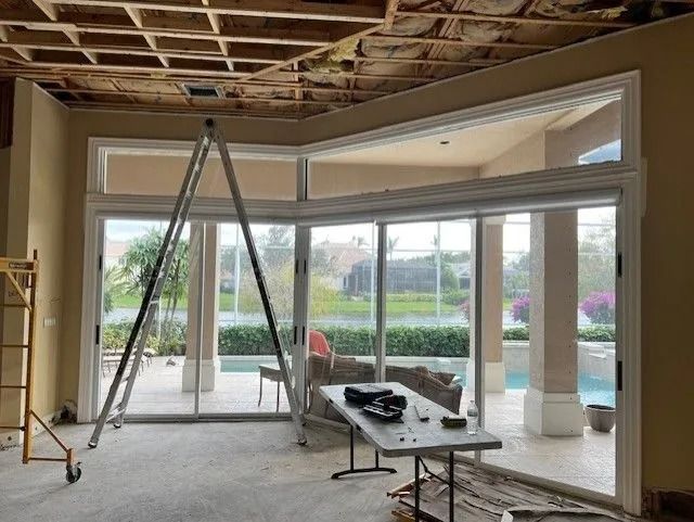 Interior view of room with large windows, scaffolding, and open ceiling during construction.
