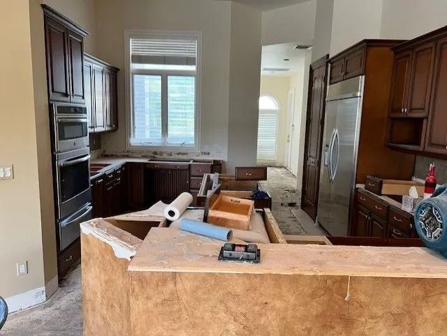 Kitchen undergoing renovation; dark cabinets, oven, and refrigerator visible. Countertop being worked on.