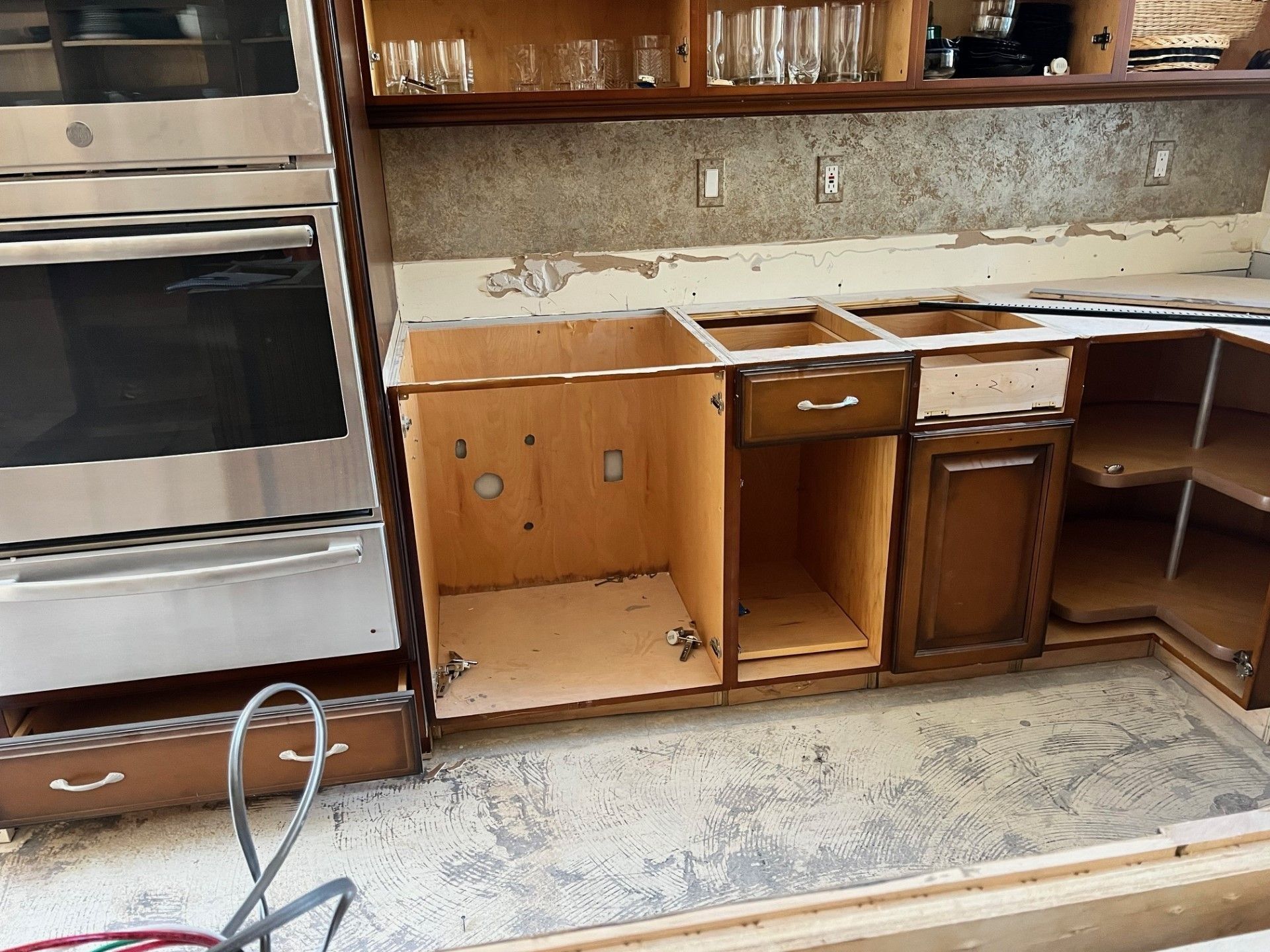 Kitchen cabinets undergoing renovation; exposed interiors, stainless steel oven, damaged countertop.