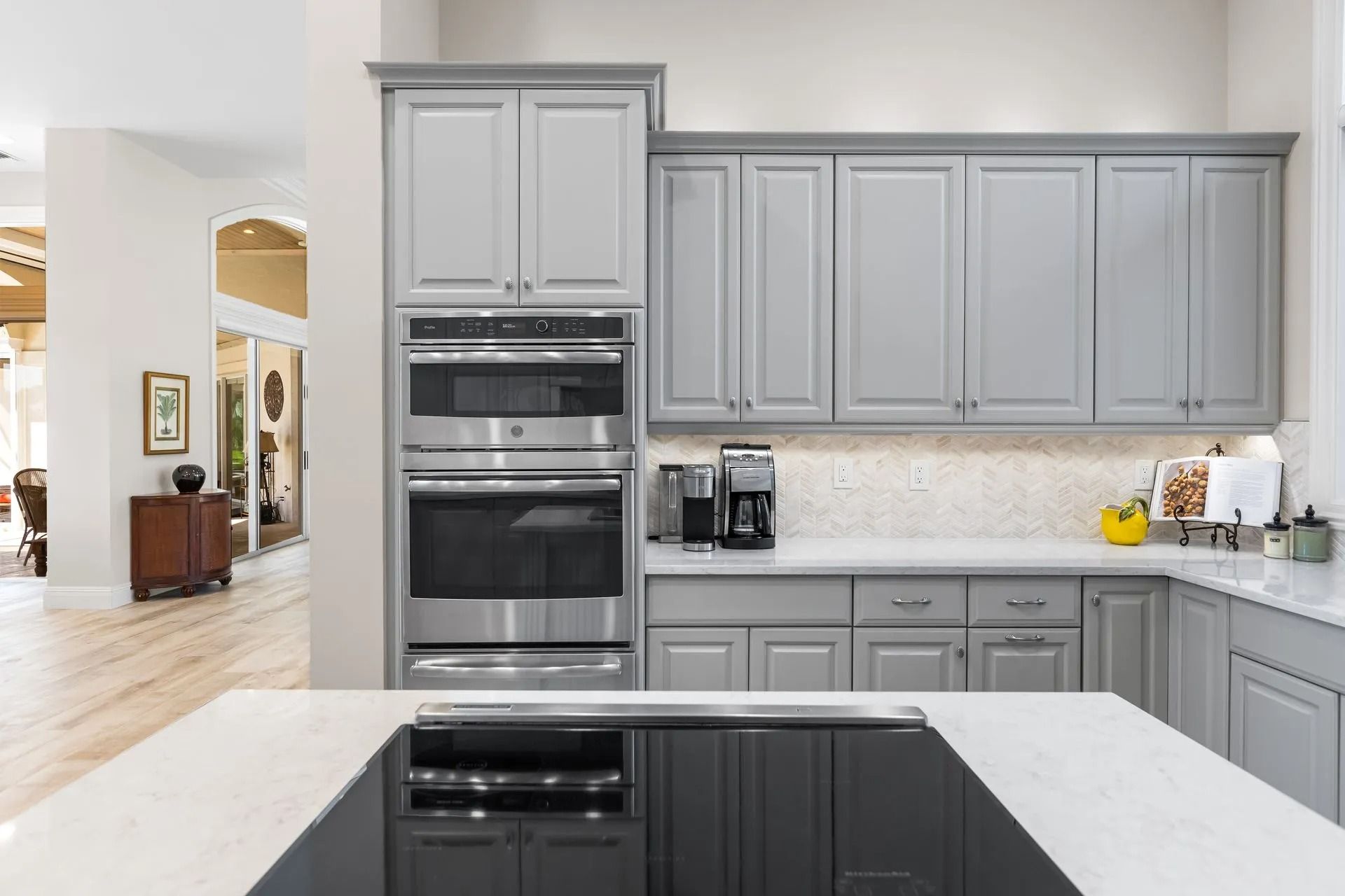 Gray kitchen cabinets with built-in ovens, countertop, and an island with a black cooktop.