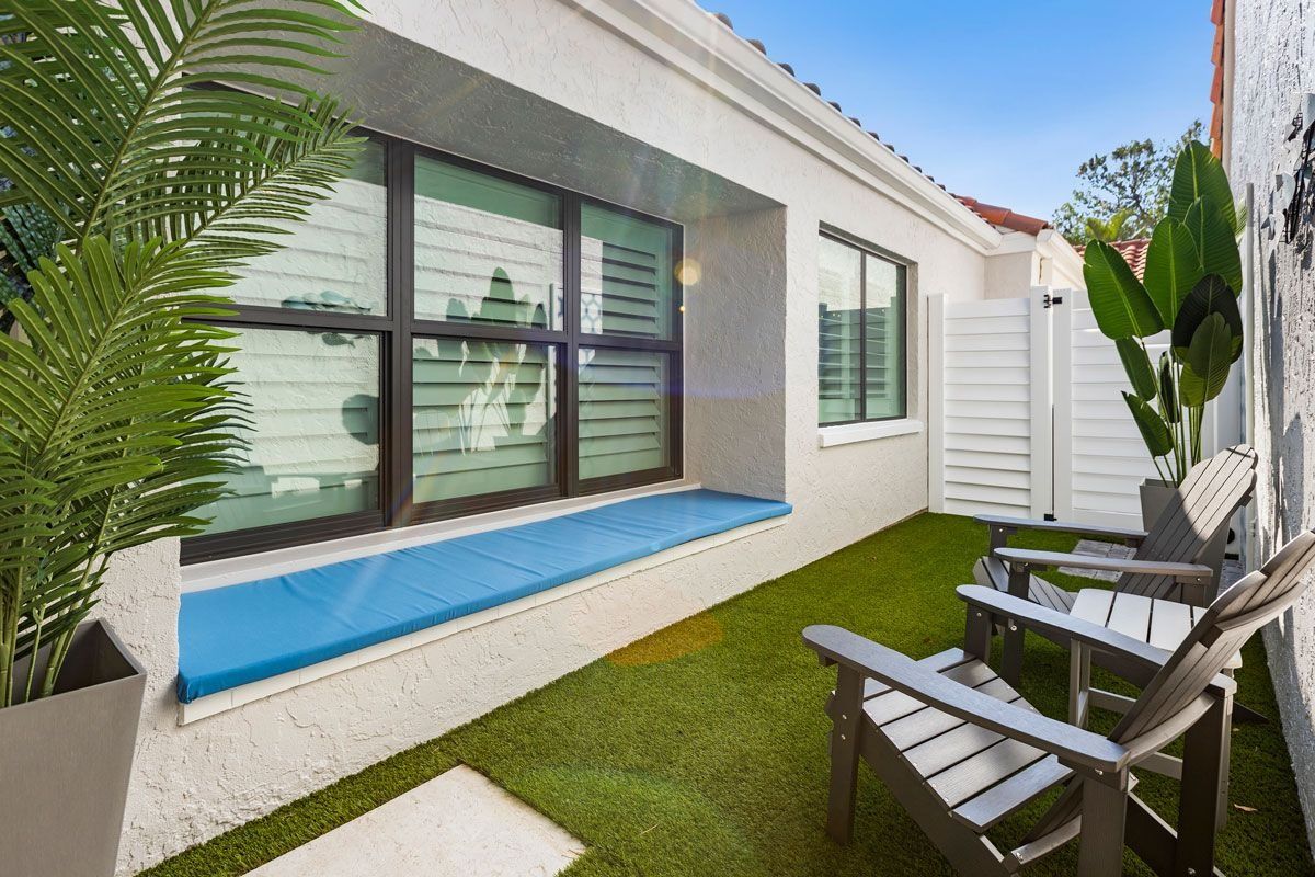 Small outdoor patio with green turf, white walls, lounge chairs, and blue window seat.