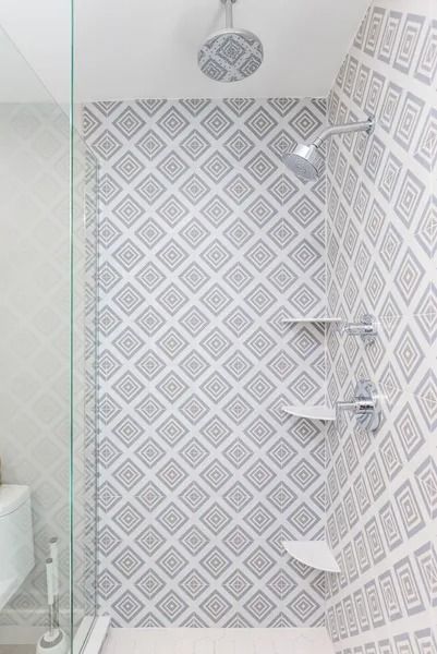 Shower with gray and white patterned tile and three white shelves.