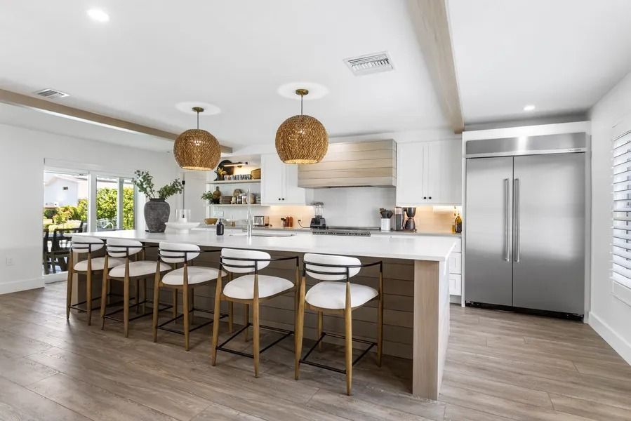 Modern kitchen with island, seating, stainless steel appliances, and two hanging woven light fixtures.