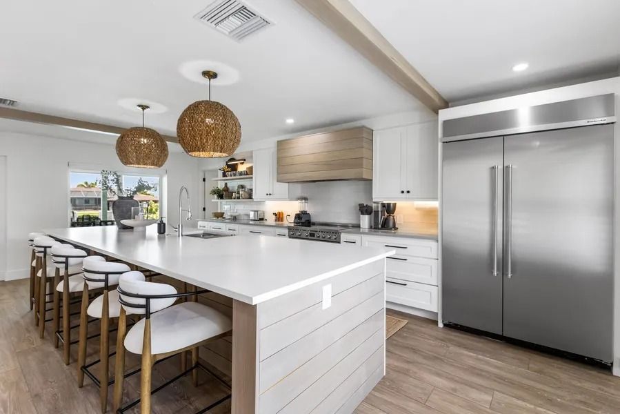 Modern kitchen with a large island, stainless steel refrigerator, and pendant lights.