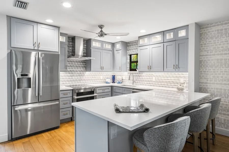 Modern gray kitchen with stainless steel appliances, white countertops, and bar seating.