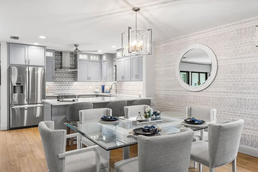 Modern kitchen and dining area with gray cabinets, glass table, and patterned wallpaper.