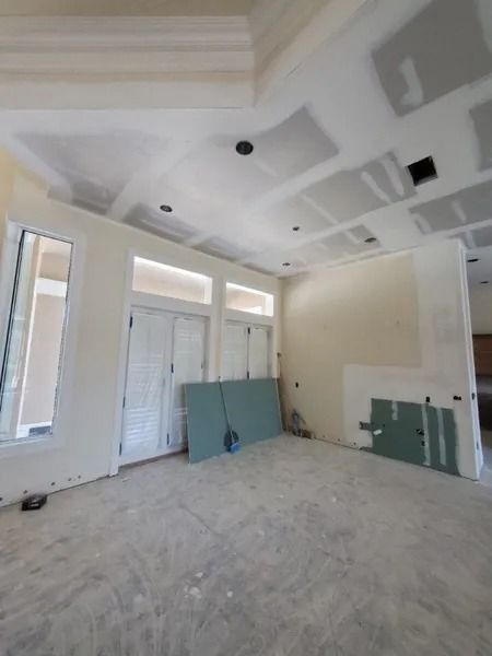 Interior room under construction, with drywall and unfinished surfaces. Light beige walls, white ceiling, and concrete floor.