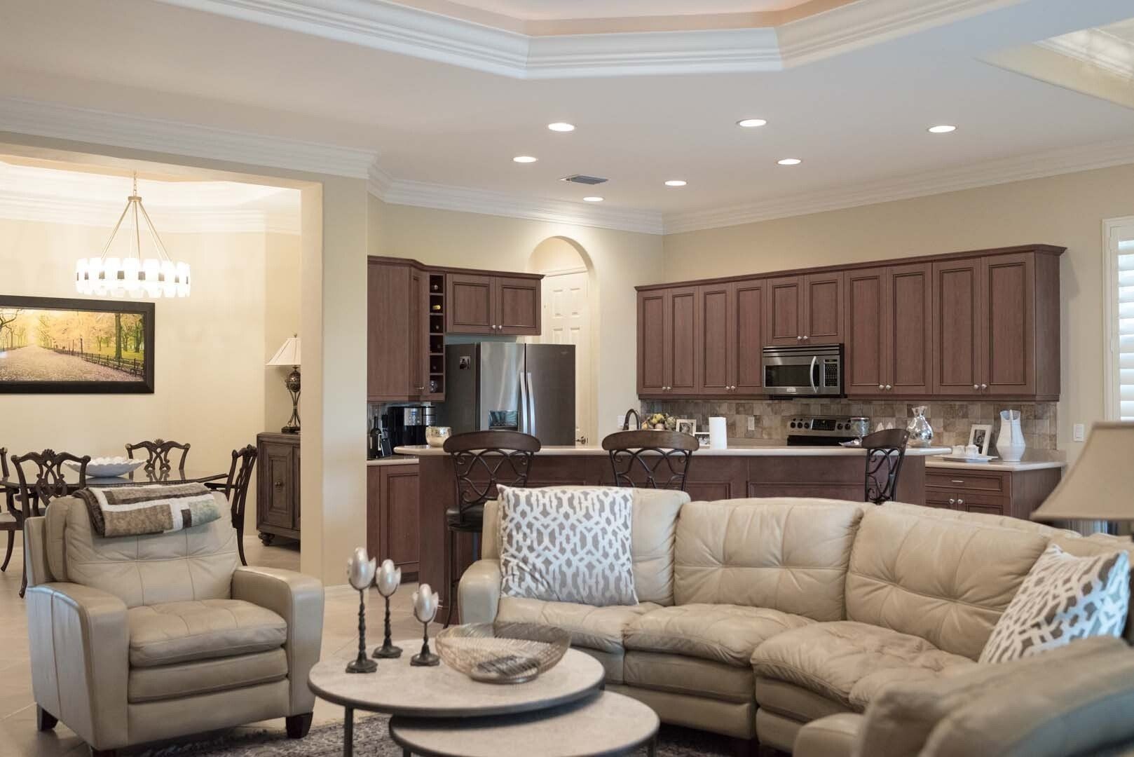 Open-concept living space with kitchen and seating area. Brown cabinets, beige sectional sofa, and round coffee tables.