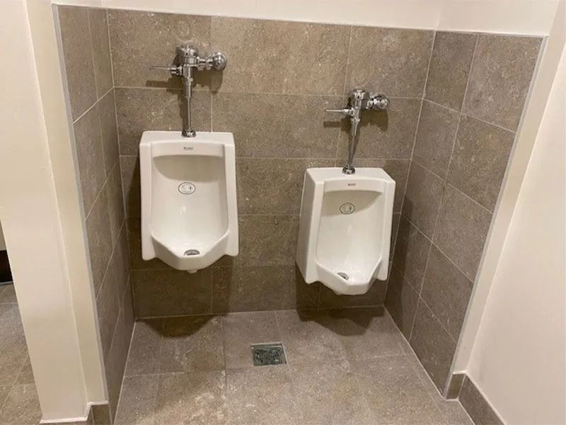 Two white urinals on a tiled wall in a public restroom.