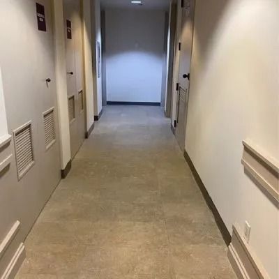 Long, beige hallway with doors on both sides. A doorway at the end emits light.