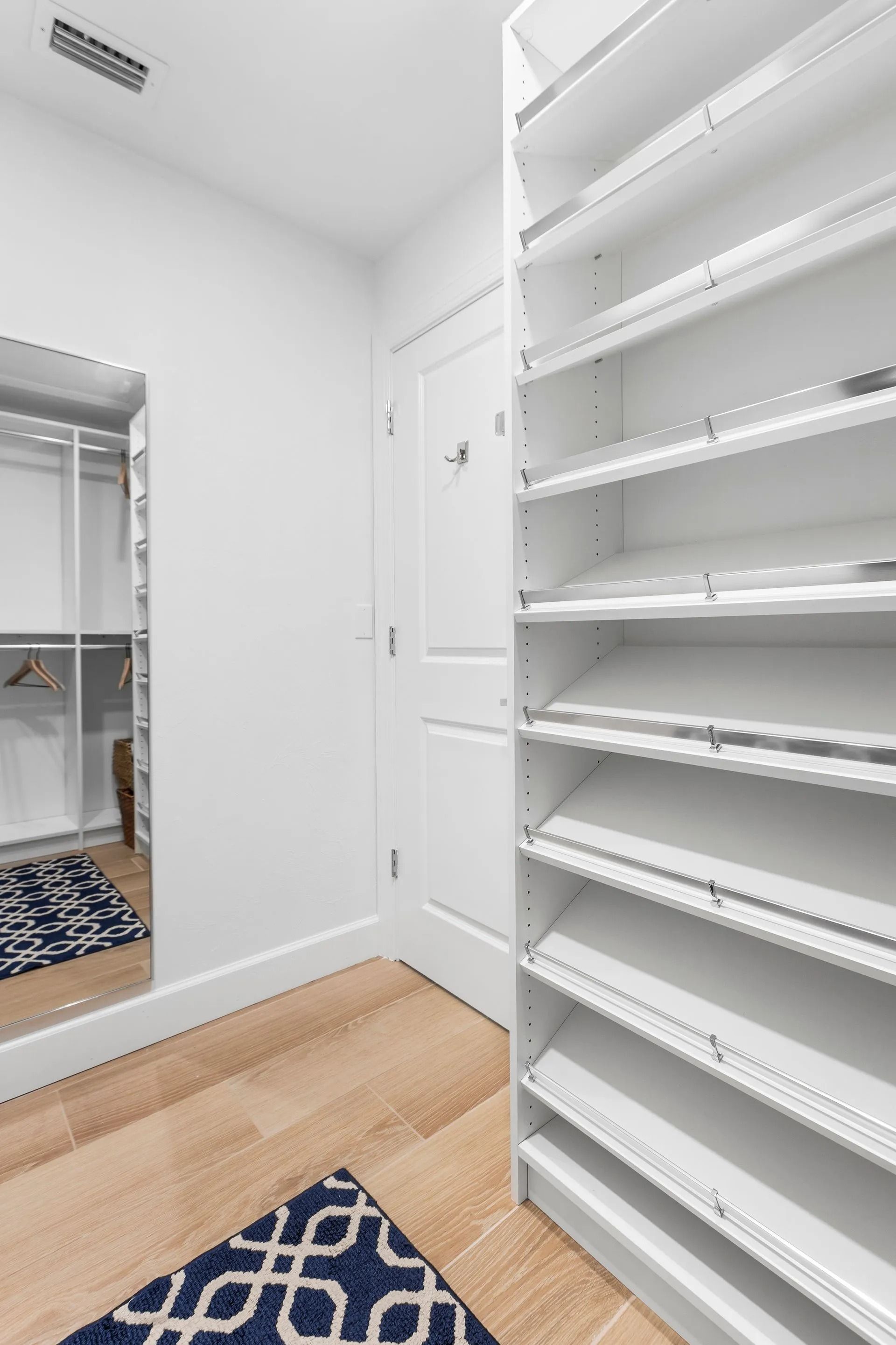 White walk-in closet with shelves and a full-length mirror, wood floor, and blue patterned rug.