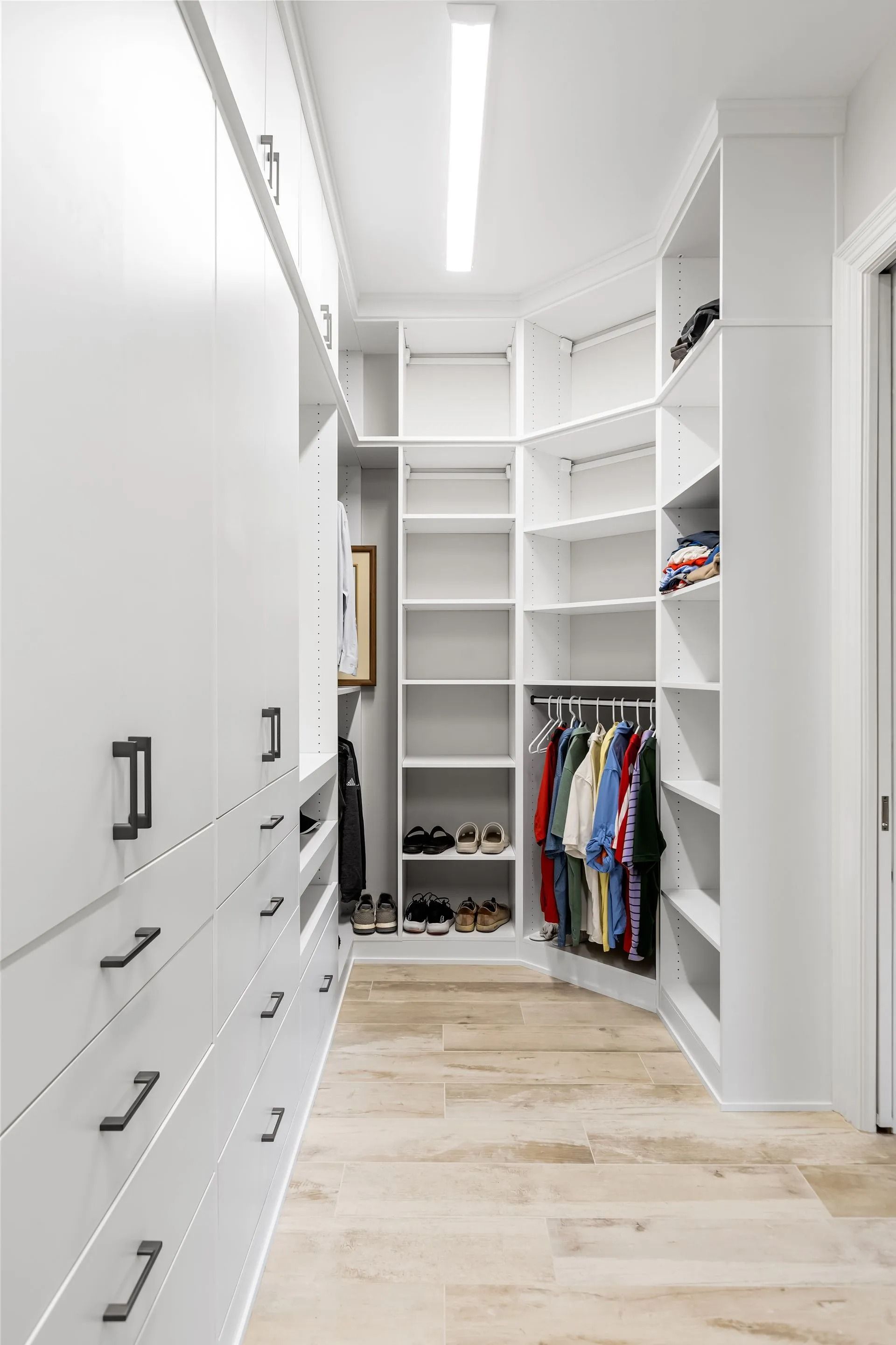 White walk-in closet with shelves, drawers, and hanging rods. Beige tiled floor, bright lighting.