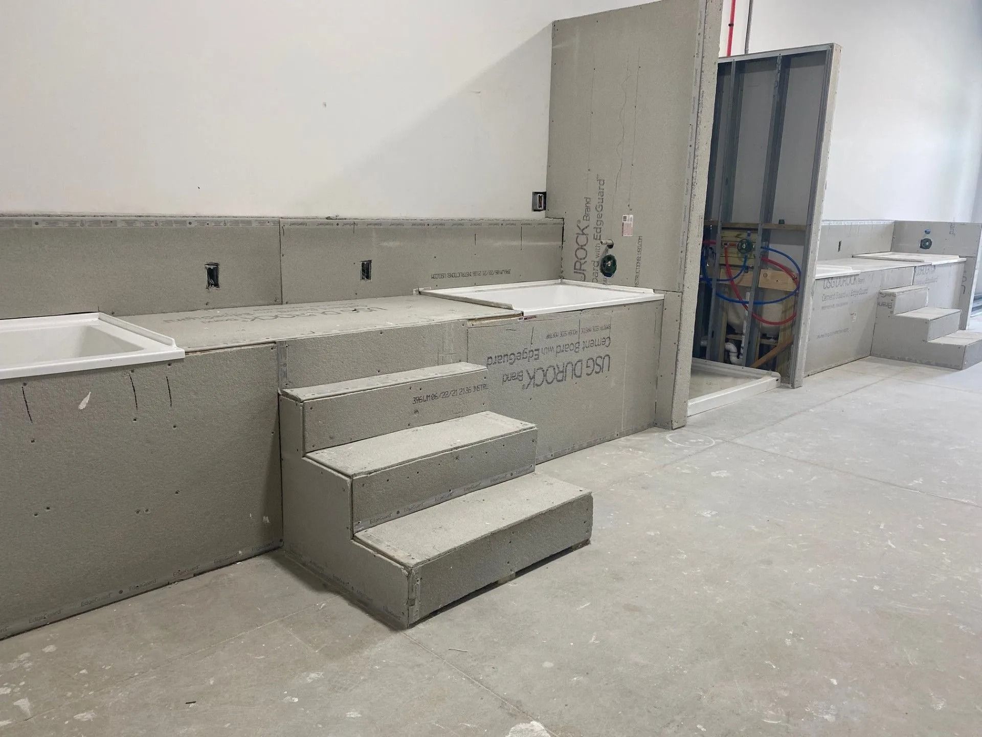 Interior under construction; grey drywall covers walls, steps, and structure; unfinished bathtub visible.